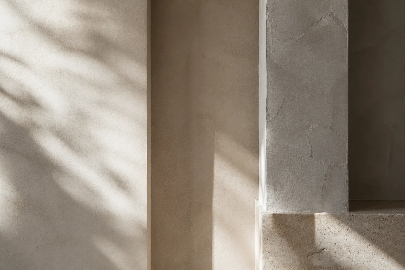 Close-up of layered plaster wall textures in warm neutral tones with oblique natural light